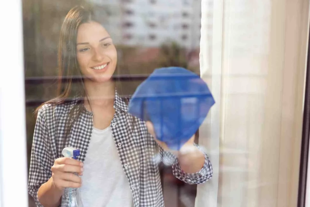 How to Clean Double Glazed Windows ?Woman cleaning a double glazed window with a blue microfiber cloth and spray bottle for a streak-free, sparkling finish.